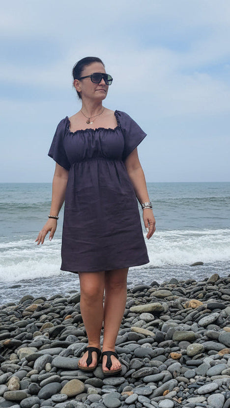 Woman in a charcoal dress standing on a pebble beach with ocean in the background
